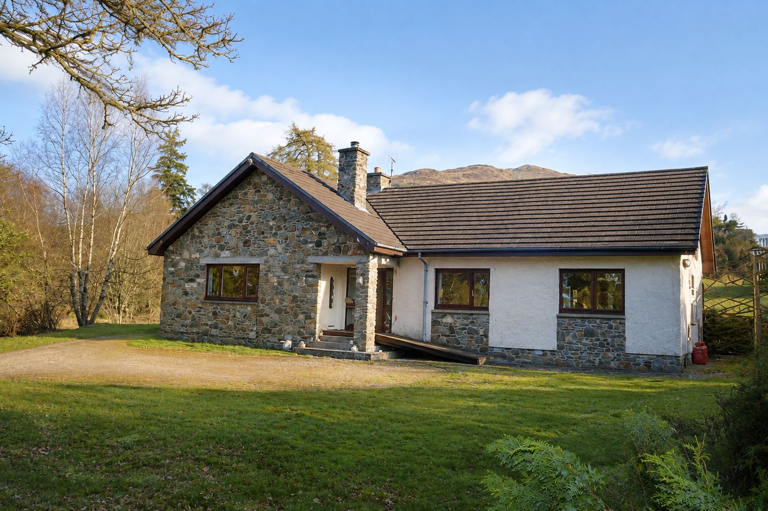 A two-story stone house with a stone chimney, a front porch, and a driveway leading to the entrance.