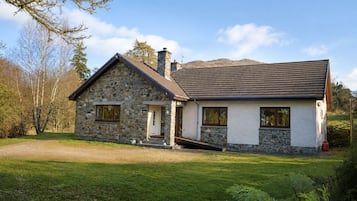 A two-story stone house with a stone chimney, a front porch, and a driveway leading to the entrance.