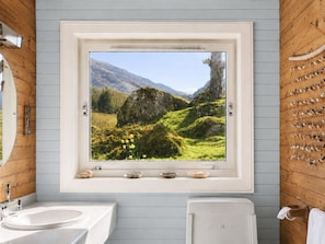 A bathroom with a large window, a sink, a toilet, and a towel rack with towels. - CRAGMHOR (Balquhidder)
