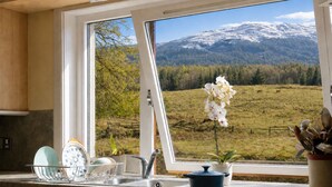 Cozinha com vista para uma paisagem montanhosa, um vaso de flores e louças sobre o balcão.