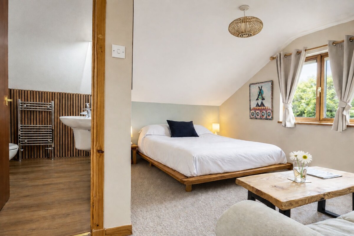 Quarto com cama, mesa de cabeceira e janela com cortinas.