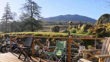 A deck with chairs and a motorcycle, overlooking a mountainous landscape with a clear sky.