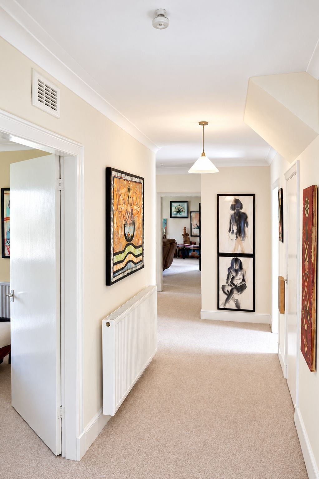 A hallway with a white door, a radiator, and artwork on the walls.