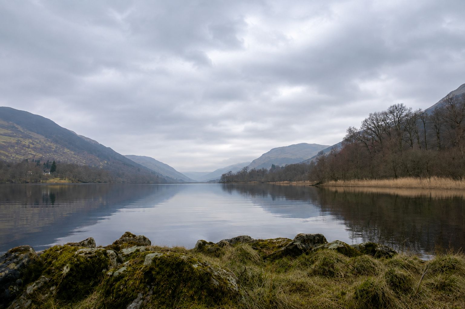 A calm lake with mountains in the background and a rocky foreground.