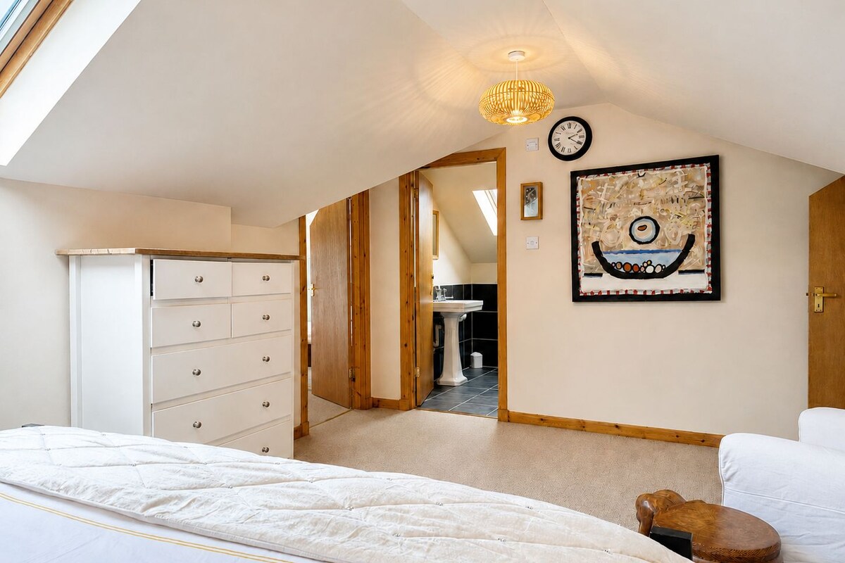 Um quarto com uma cama, cômoda, relógio, quadro e porta que dá para outro espaço.