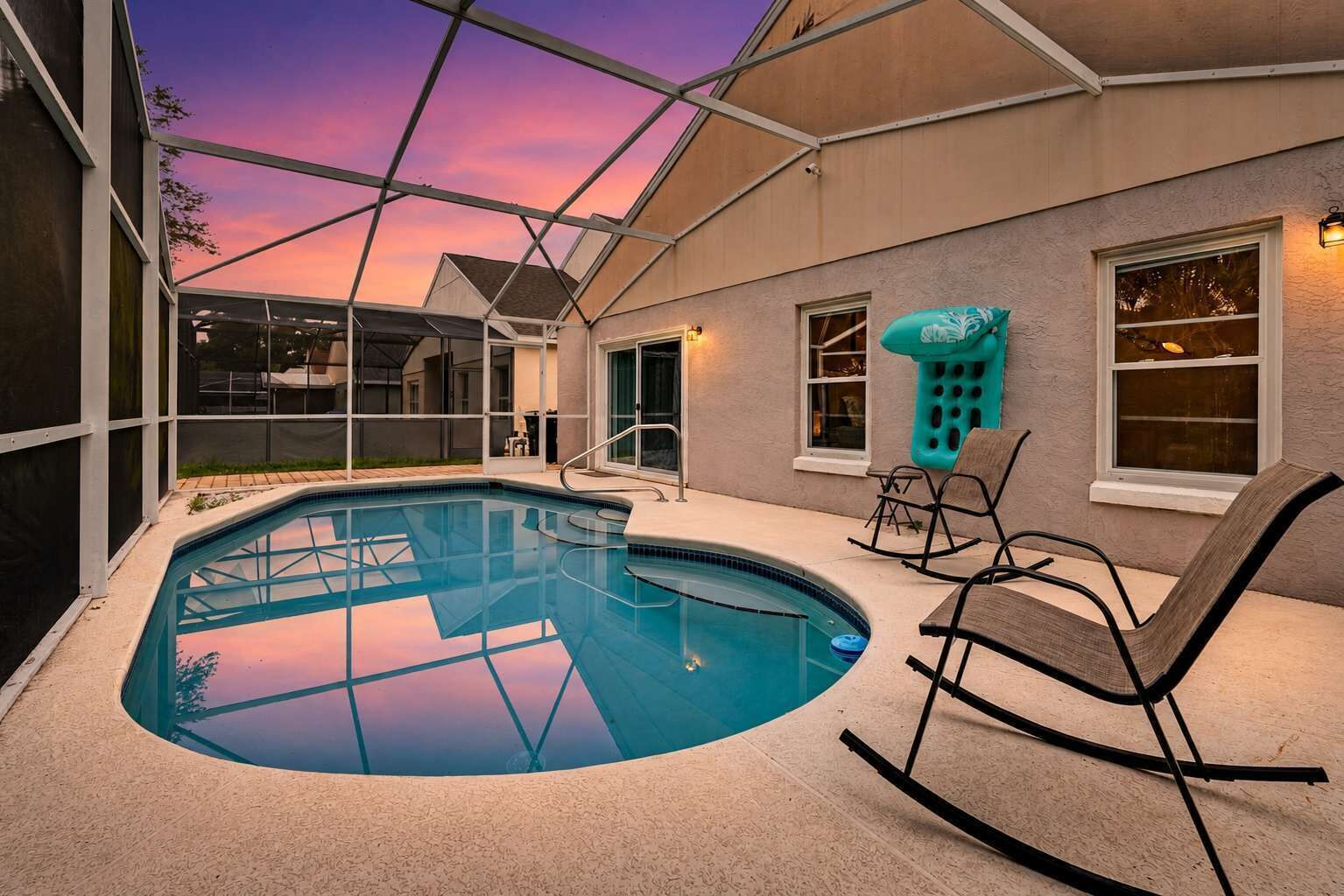 A swimming pool with a clear view of the sky, surrounded by a covered patio area with chairs and a window.