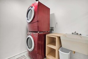 A compact laundry room with a red washing machine and dryer, a wooden shelf, and a sink. - Chatham Park Private Pool Retreat (Kissimmee)