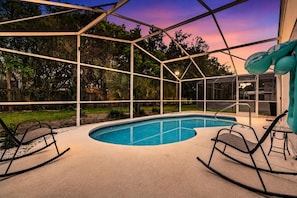 A swimming pool with a glass enclosure, surrounded by chairs and a lamp. - Chatham Park Private Pool Retreat (Kissimmee)