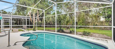 Una piscina con agua azul cristalina, rodeada por una valla de metal blanco y un césped con árboles al fondo.