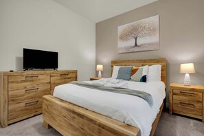 A bedroom with a bed, wooden nightstands, a television, and a painting on the wall. - 5BR Disney Escape with Pool and Game Room (Kissimmee)