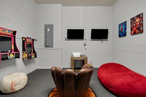 A room with two arcade machines, a television, a bean bag, and a red couch. - 5BR Disney Escape with Pool and Game Room (Kissimmee)