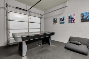 A room with a pool table, a grey couch, and four superhero-themed paintings on the wall. - 5BR Disney Escape with Pool and Game Room (Kissimmee)