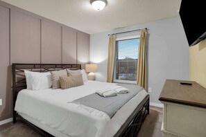 A bedroom with a bed, bedside lamp, window with blinds, and a TV mounted on the wall. - 5BR Disney Escape with Pool and Game Room (Kissimmee)