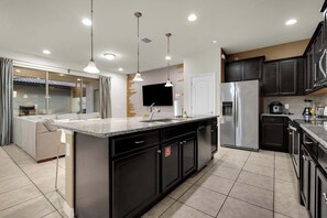 A modern kitchen with a central island, dark cabinetry, and a built-in dishwasher. - 5BR Disney Escape with Pool and Game Room (Kissimmee)