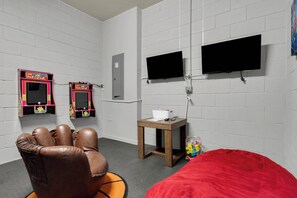 A room with two arcade machines, a bed with a red cover, a small table with a white container, and two mounted televisions. - 5BR Disney Escape with Pool and Game Room (Kissimmee)
