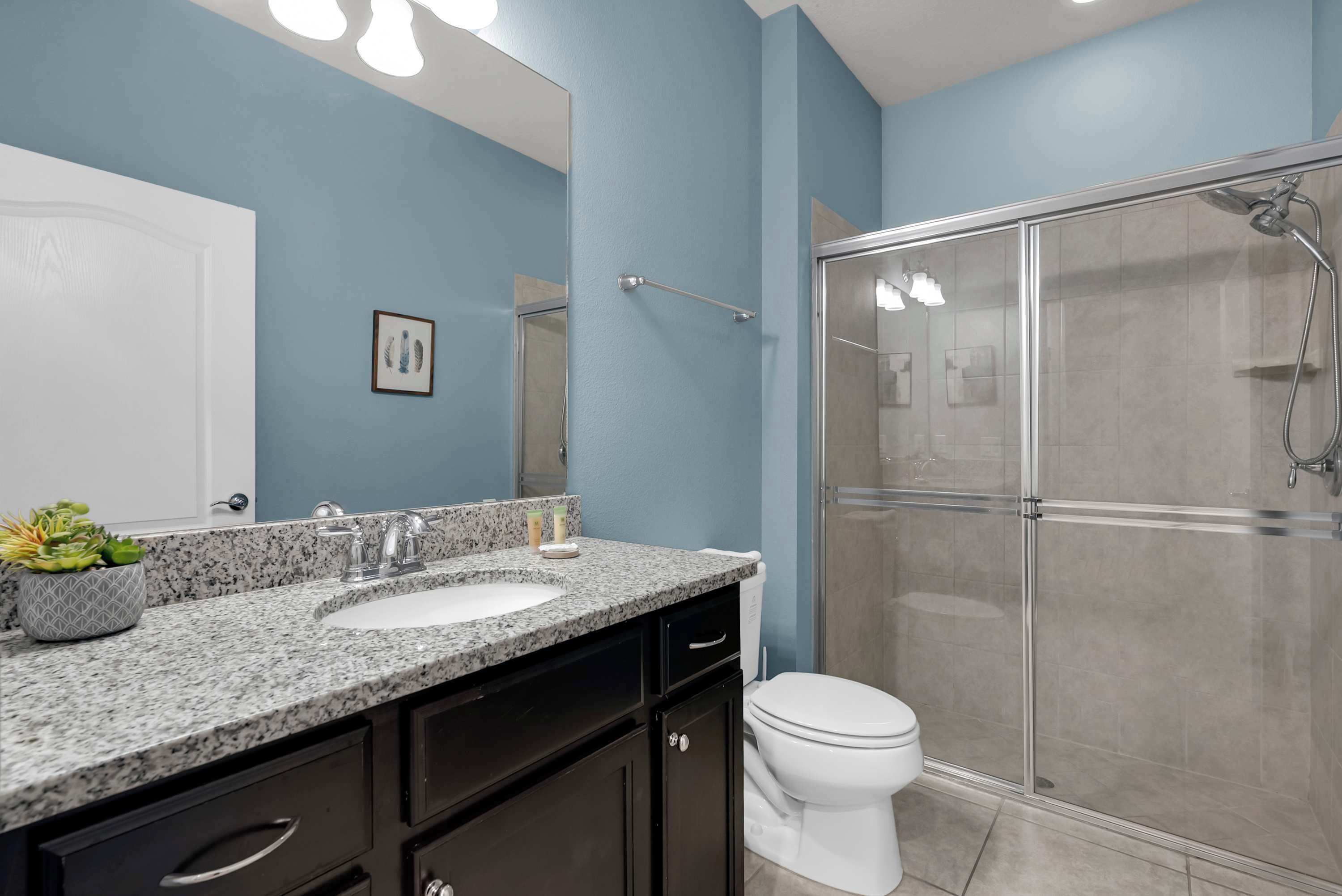 Une salle de bain moderne avec un comptoir en granit, un lavabo blanc, une cabine de douche en verre et des toilettes.