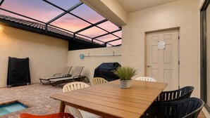 Un patio al aire libre con mesa y sillas de madera, una piscina pequeña y una zona de parrilera techada.
