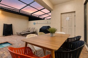 An outdoor patio with a wooden table and chairs, a small pool, and a covered grill area. - 5BR Disney Escape with Pool and Game Room (Kissimmee)