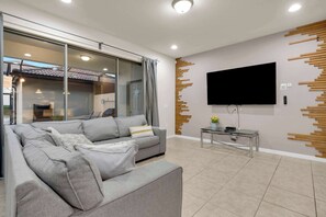 A modern living room with a grey sofa, a flat-screen TV mounted on the wall, and a glass coffee table. - 5BR Disney Escape with Pool and Game Room (Kissimmee)