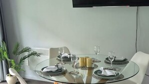 Un tavolo di vetro rotondo con sedie bianche, una televisione a schermo piatto montata a parete e una pianta in vaso a sinistra.