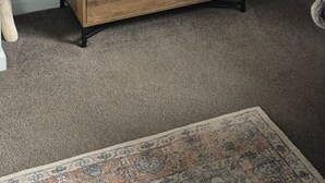 Un comò di legno con tre cassetti, un vaso bianco con pannocchie di giunco e uno specchio decorativo a parete.