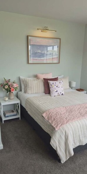 A bedroom with a bed, a nightstand, a vase with flowers, and a framed picture on the wall. - Walk to Stadium + 2 Free Car Parks Prime Location (Christchurch)