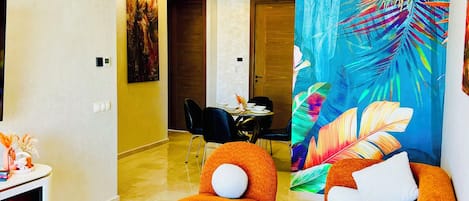 Un salon moderne avec une cheminée, une table basse ronde, un canapé et une fresque murale aux couleurs vives représentant un paysage tropical.