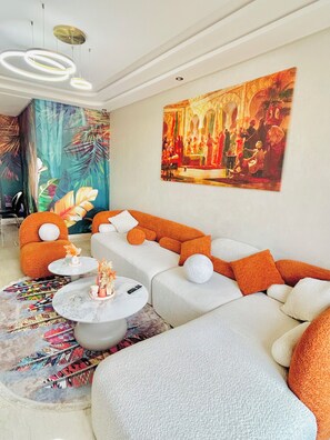 Een moderne woonkamer met een hoekbank, een ronde salontafel en een kleurrijk abstract schilderij aan de muur.