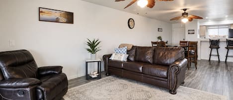 Un salon avec un canapé en cuir marron, un tapis à motifs et deux ventilateurs de plafond.