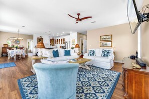 A spacious living room with a ceiling fan, a dining area with a chandelier, and a kitchen in the background. - The Crane Cottage, Bayfront, Private Pool, Private Dock (St. George Island)