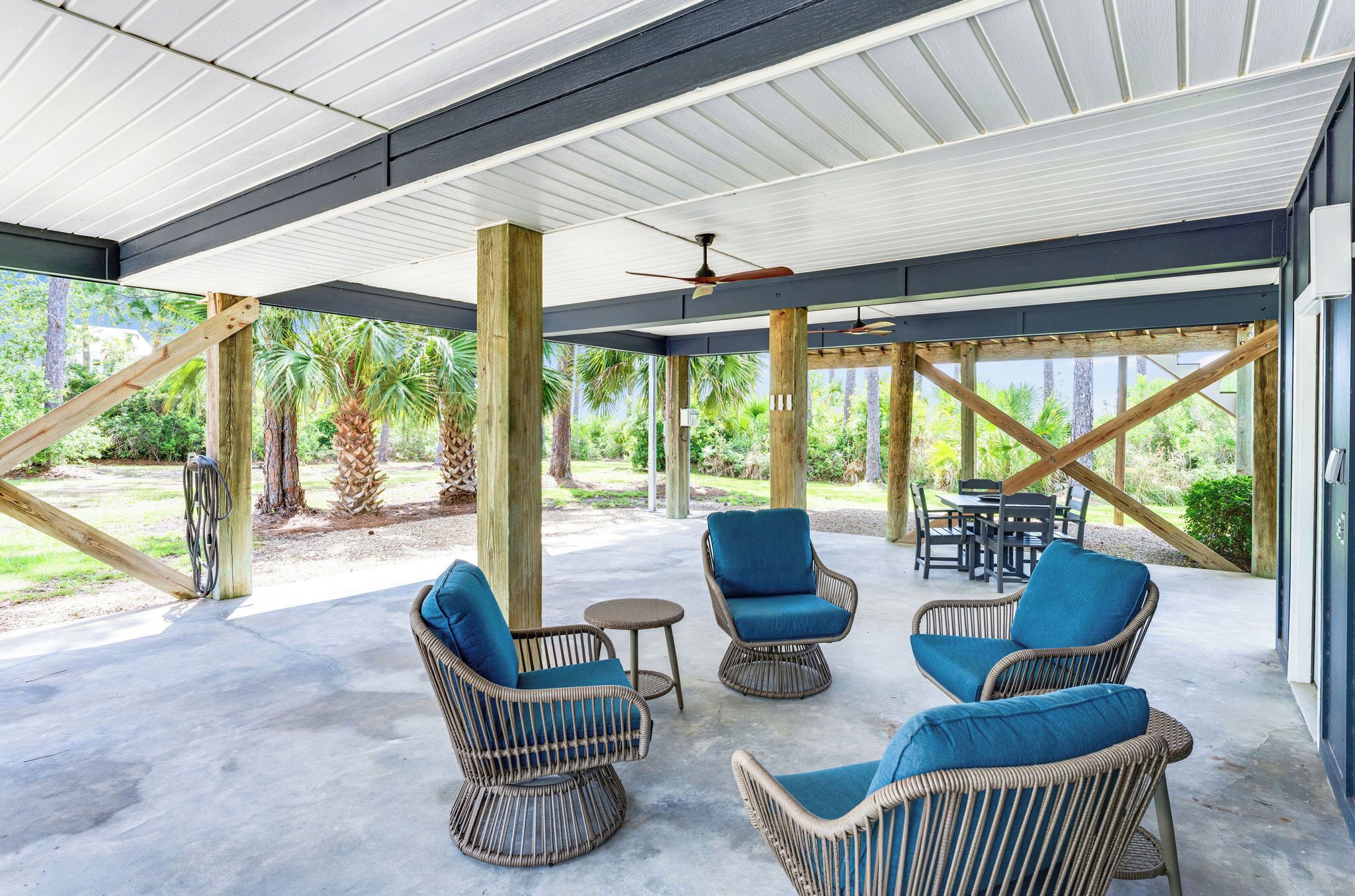 An outdoor covered patio with wicker furniture, ceiling fans, and a view of the surrounding greenery.