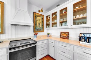 A kitchen with white cabinetry, a stove, and a coffee machine. - The Crane Cottage, Bayfront, Private Pool, Private Dock (St. George Island)