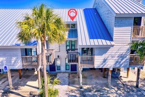 A two-story building with a red logo, a balcony, and a palm tree. - Ocean Mile A-2, Pool Front with Unobstructed Beach View, Boardwalk (St. George Island)