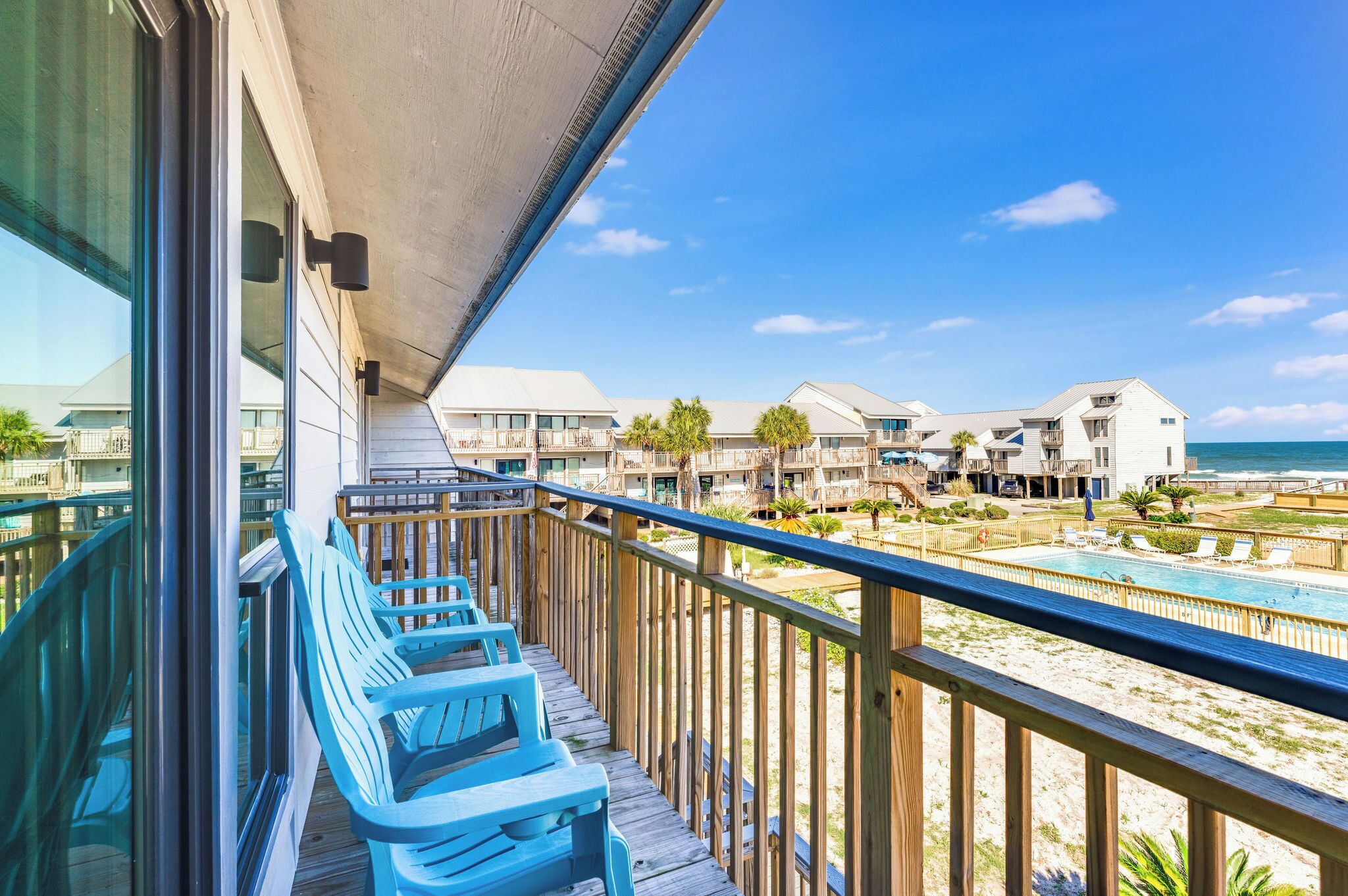 A balcony with blue chairs overlooking a beach and a pool area.
