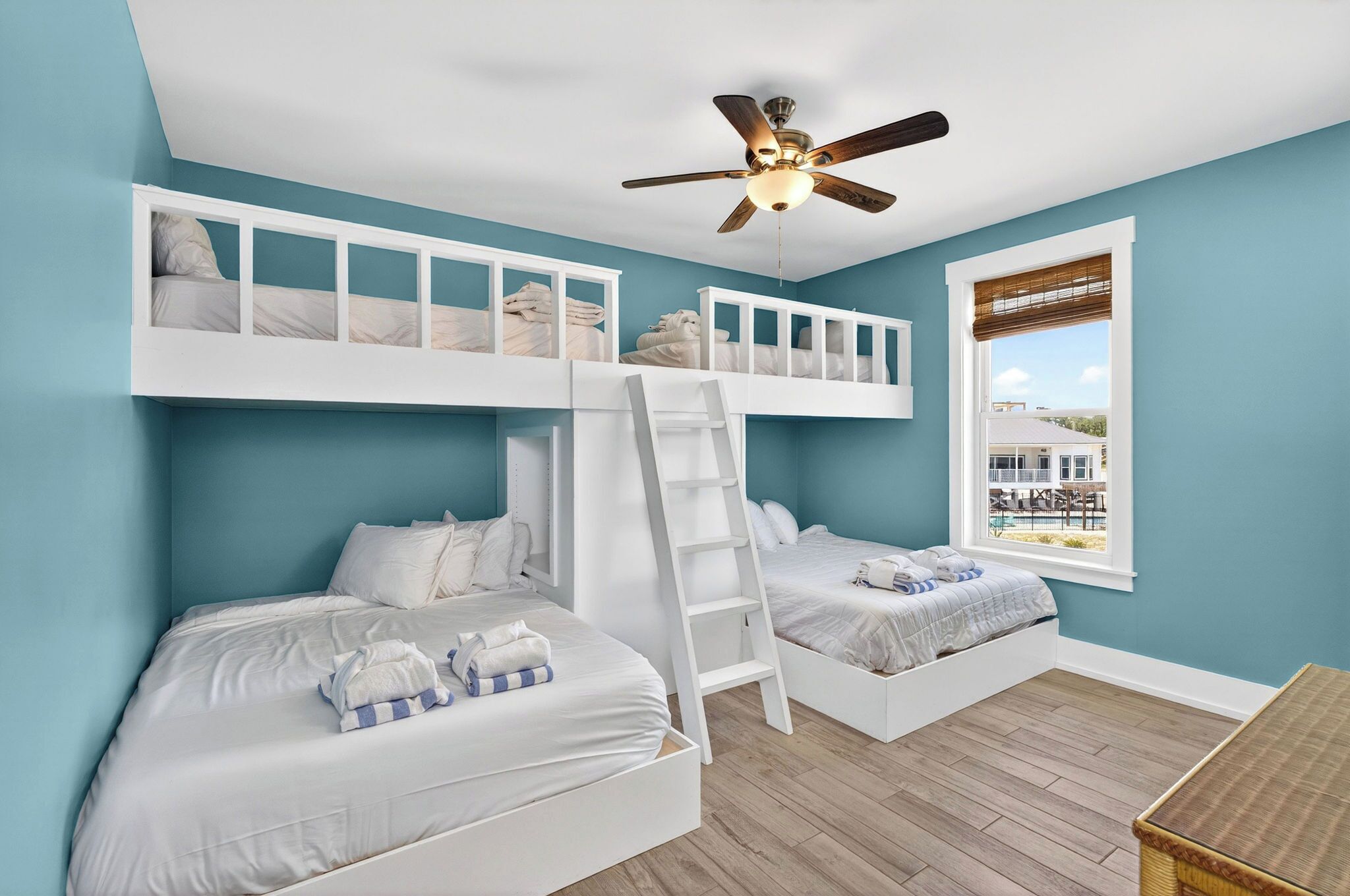 A room with two bunk beds, a ceiling fan, and a window with a view of a pool.