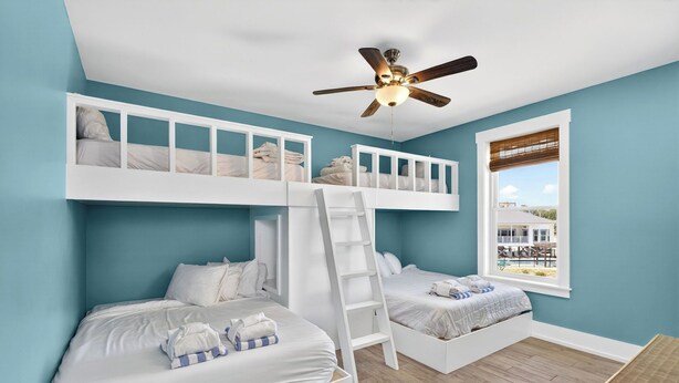 Una habitación con dos literas, un ventilador de techo y ventana con vista a una piscina.