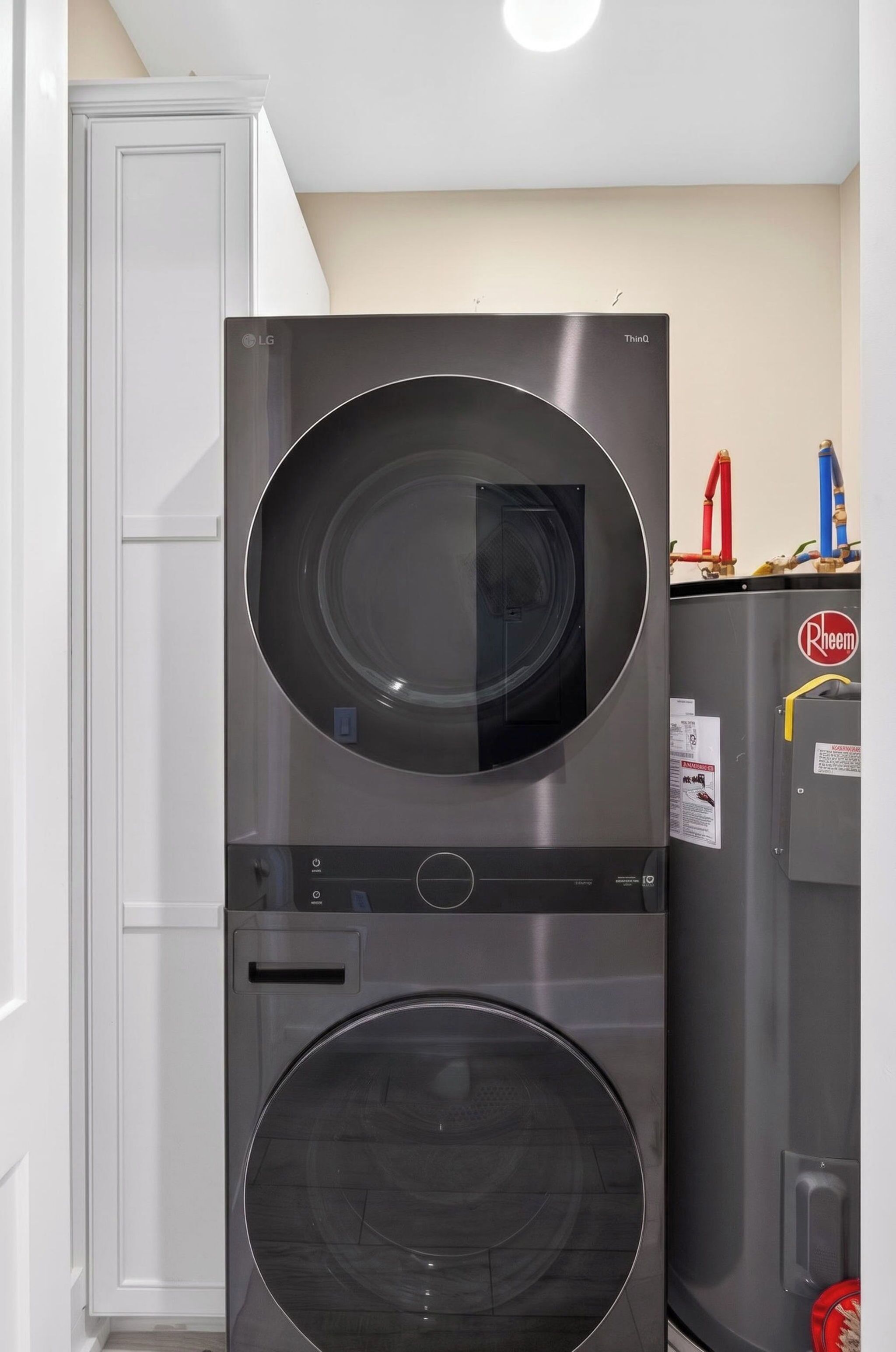 Un appareil combiné lave-linge et sèche-linge, de type « empilable », avec un panneau de commande et un chauffe-eau situés sur le dessus.
