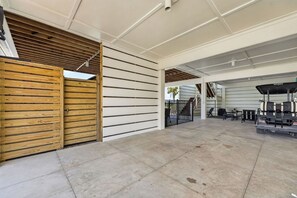 An open-air covered area with a wooden gate, a seating area with tables and chairs, and a view of a staircase leading to an upper level. - Gulf Watch! Across street from beach, private pool, elevator, and more! (St. George Island)