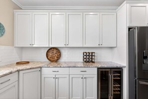 A kitchen with white cabinets, a stainless steel refrigerator, and a herringbone-patterned wooden tray on the countertop. - Gulf Watch! Across street from beach, private pool, elevator, and more! (St. George Island)