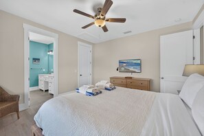 A bedroom with a bed, a ceiling fan, a dresser, a television, and a door leading to another room. - Gulf Watch! Across street from beach, private pool, elevator, and more! (St. George Island)