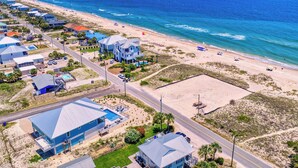 Vista aérea de una zona residencial costera con casas, una playa y un cielo azul despejado.