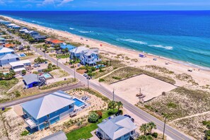 An aerial view of a coastal residential area with houses, a beach, and a clear blue sky. - Gulf Watch! Across street from beach, private pool, elevator, and more! (St. George Island)
