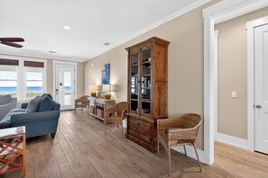 A spacious living area with a sofa, chairs, a wooden cabinet, and a view of the ocean. - Gulf Watch! Across street from beach, private pool, elevator, and more! (St. George Island)