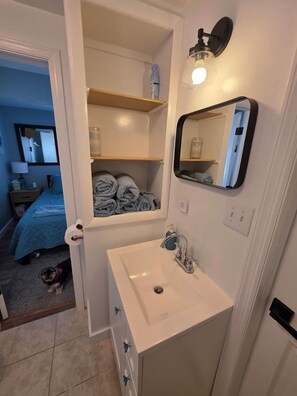 Een badkamer met een wit wastafel, een spiegel en een plank met handdoeken.