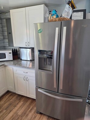 A stainless steel refrigerator with a water dispenser, white cabinetry, and a microwave on a granite countertop. - Barking Bayside Bungalow (Lower Township)