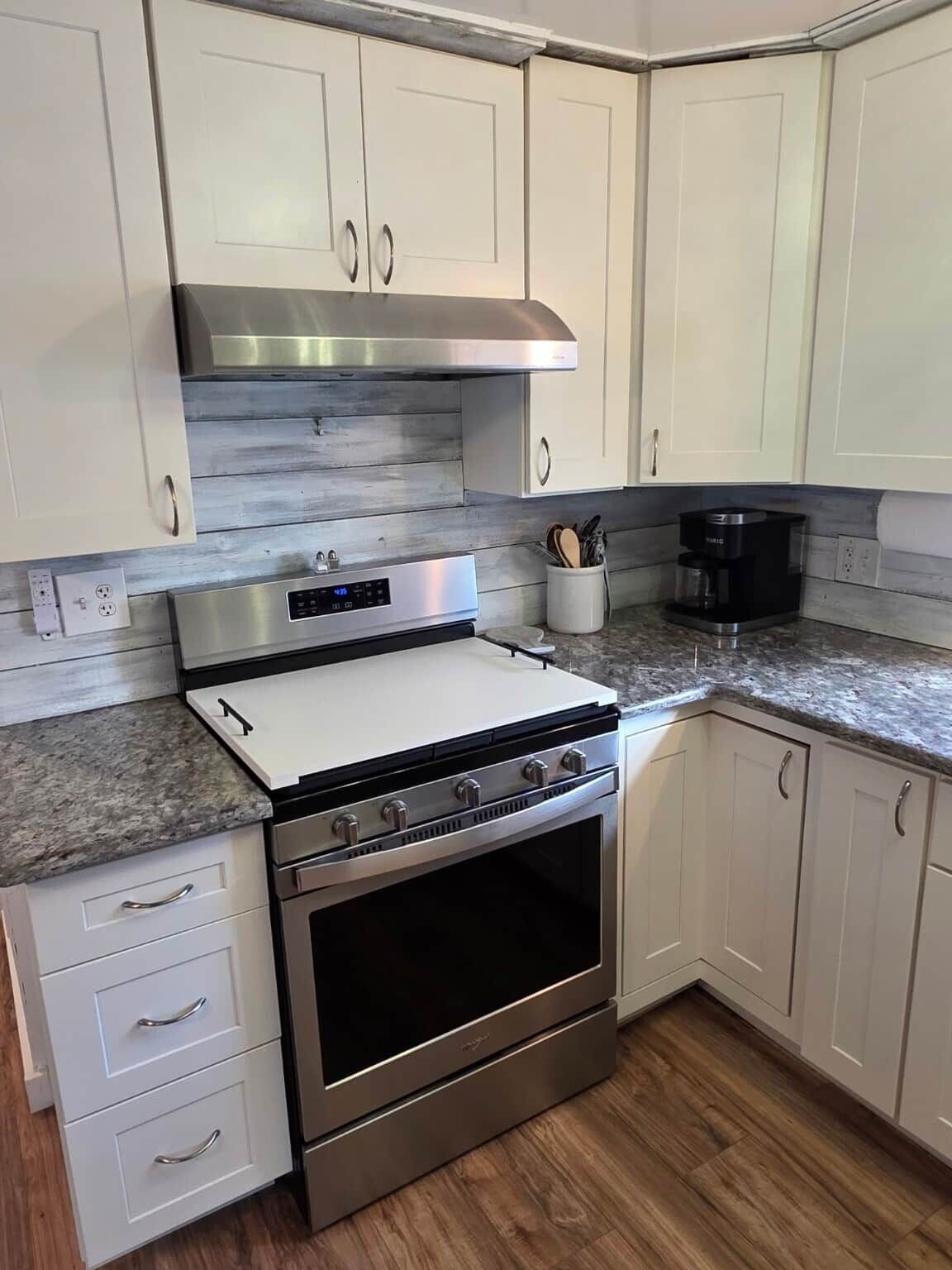 A kitchen with white cabinets, a stainless steel range hood, a built-in oven, and a granite countertop.