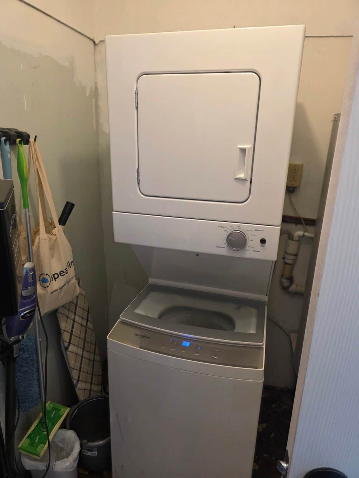 A compact washer and dryer unit in a small laundry room with a visible control panel and a bag hanging nearby.