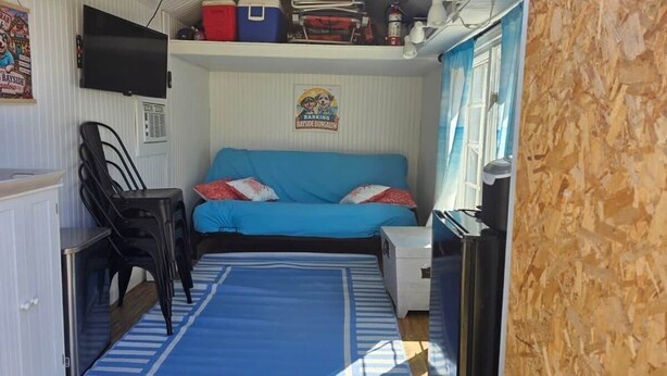 Ein gemütlicher Raum mit einem blauen Sofa, einem kleinen Tisch und einem an der Wand befestigten Fernseher.
