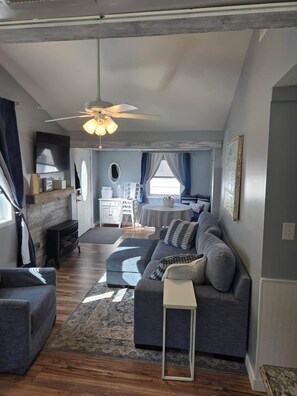 A modern living room with a grey sofa, a small side table, a ceiling fan, and a fireplace. - Barking Bayside Bungalow (Lower Township)