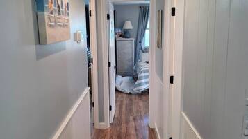 Un couloir avec un tapis à motifs, un tableau accroché au mur et une porte donnant sur une chambre à coucher.
